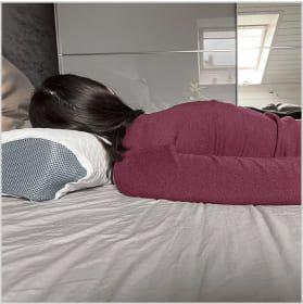 Person lying face down on a bed with a pillow under their head.
